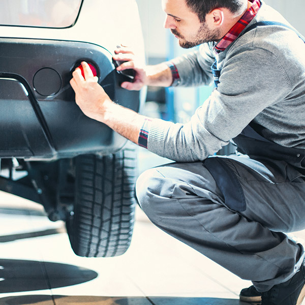 car mechanic kneeling next to rear bumper of the vehicle and installing red reflector